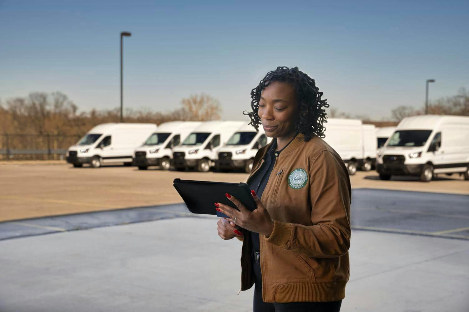 Woman holding an ipad with a fleet of vans behind her